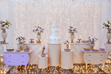 a table decorated with wedding sweets LED lights in the background, with a wedding cake in the center