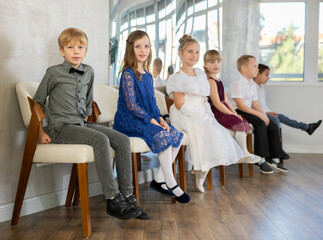Happy children in festive clothes sit on chairs waiting for ballroom dancing to start