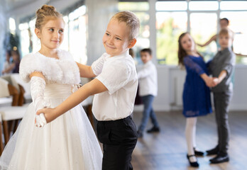Fototapeta na wymiar Positive little boys and girls in festive clothes dancing pair dance in the ballet studio