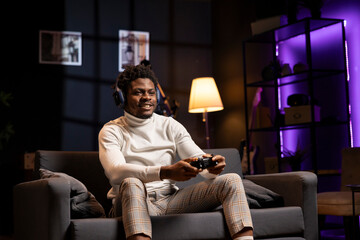 Happy man having fun while playing videogames on gaming console with teammates, talking through...