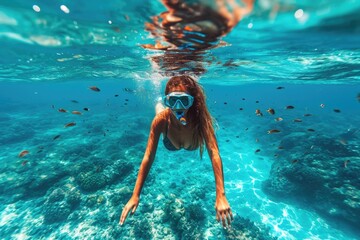 A daring diver gracefully glides through the crystal clear water, surrounded by colorful fish, as she embraces the freedom and exhilaration of underwater exploration in her sleek swimsuit and essenti - obrazy, fototapety, plakaty