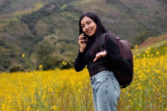 Retrato de una hermosa chica turista charla en el móvil en el hermoso paisaje, revisando teléfono inteligente en aire libre,una chica usando el móvil en medio de un camino rodeado de flores y montaña