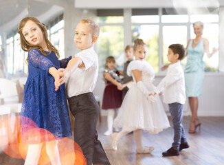 Positive little boys and girls in festive clothes dancing pair dance in the ballet studio