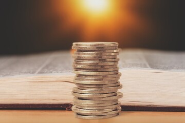 Stack of coins and Holly Bible book on background