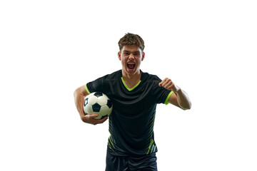Portrait of emotional young man in black uniform, soccer player with ball emotionally shouting isolated over white background with grass flooring. Concept of sport, game, competition, active lifestyle
