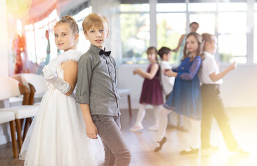 Happy little children in elegant dresses practicing rock-n-roll dance with teacher in school hall