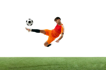 Champion. Young guy, soccer player in orange uniform training, hitting ball with leg isolated over white background with grass flooring. Concept of sport, competition, championship, active lifestyle