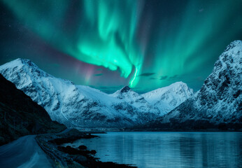 Northern lights over the snowy mountains, frozen sea, reflection in water at winter night in...