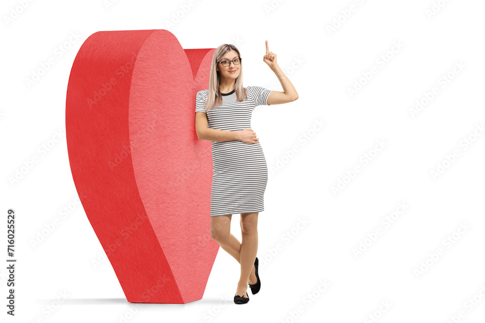 Poster Full length portrait of a young woman leaning on a red heart and pointing thumb up