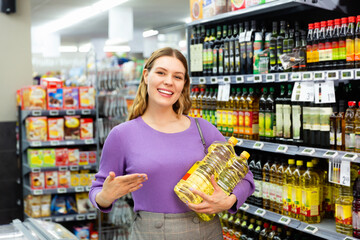 Portrait of young glad cheerful smiling woman satisfied with purchased vegetable oil in supermarket