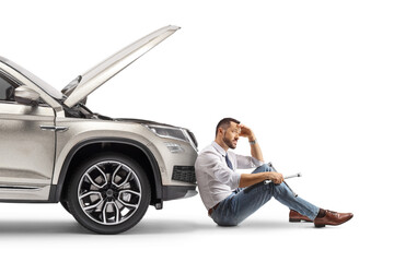 Unhappy driver sitting on the ground in front of a SUV with open hood