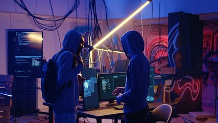 Hooded criminals in ghetto underground place discussing ways to evade getting caught by police after stealing data from victims using malware, brainstorming ways to hide their online activity