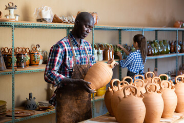 Focused African potter working at pottery studio, checking finished clay products