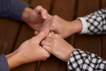 Close up on a man and a woman holding hands at a wooden table. Loving couple holding hands on...