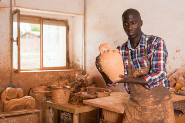Focused African potter working at pottery studio, checking finished clay products