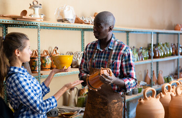 African American shopman consulting woman visitor in pottery shop