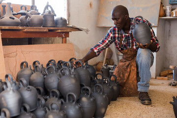 Focused African potter working at pottery studio, checking finished clay products