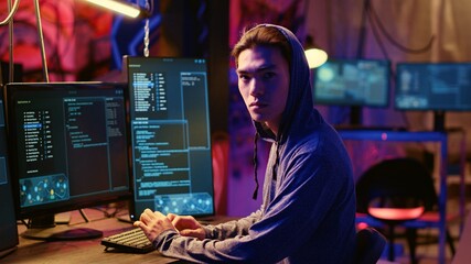 Portrait of asian hacker building spyware software designed to gather information from users computers without their knowledge. Man doing cybercriminal activities in rundown hideout