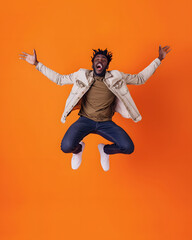 Full length portrait of cheerful african american man jumping against orange background