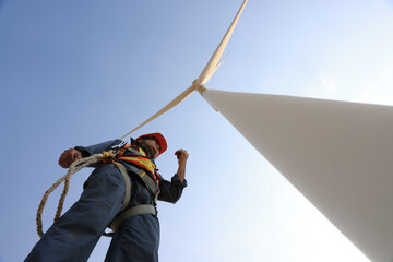 Windmill worker with safety harness and PPE working under wind turbine 
