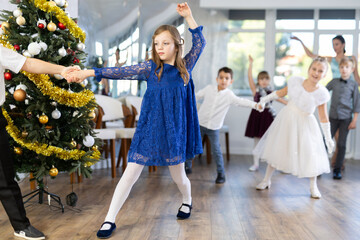 Obraz premium Beautifully dressed little boys and girls dance couple twist dance at Christmas ball near the New Year tree
