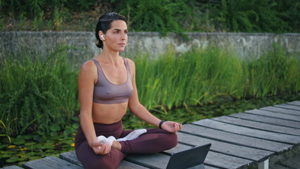 Tranquil yogini meditating tablet on park bench. Woman lotus pose watching tab