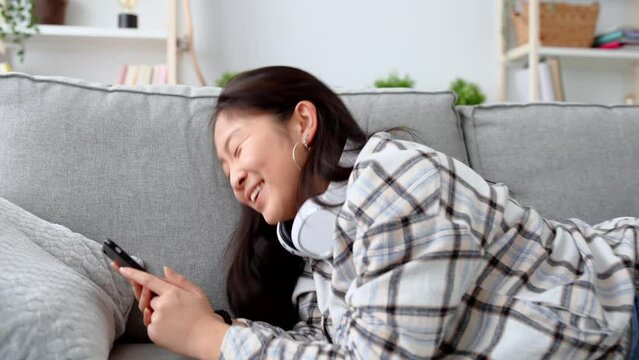 Young woman using phone on sofa. Asian teenager chatting on social media while lying on sofa.