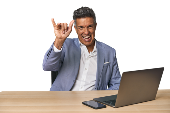 Elegant businessman at desk with laptop showing a horns gesture as a revolution concept.