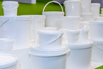 Lots of new white unmarked plastic containers and buckets for storing and transporting food and liquids. Packaging material at a fair or in a store © hodim