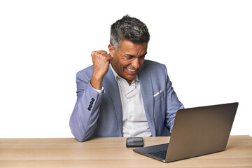 Celebratory middle-aged Hispanic man with laptop on phone call