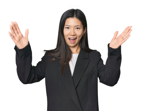 Young Chinese woman in business suit receiving a pleasant surprise, excited and raising hands.
