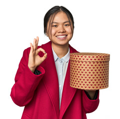 Young Chinese woman holding a heart-filled box cheerful and confident showing ok gesture.