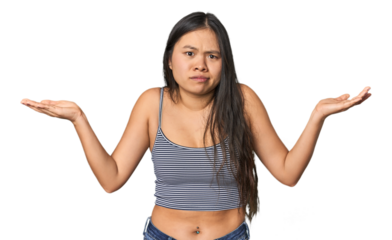 Young Chinese woman in gray top, studio doubting and shrugging shoulders in questioning gesture.