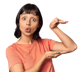 Young Hispanic woman with short black hair in studio shocked and amazed holding a copy space between hands.
