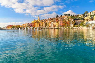 Tuinposter A small group of sailboats pass in front the old town and Les Sablettes Beach and promenade along the Cote d'Azur French Riviera at Menton, France. © Kirk Fisher