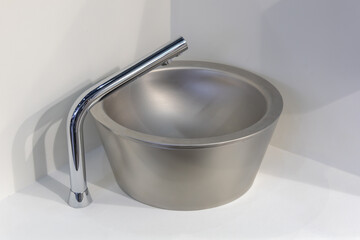 A modern round steel washbasin on a light countertop. The chrome faucet goes well with the design of the sink. Both elements look stylish and minimalist, ideal for a modern bathroom interior