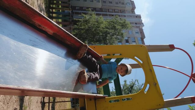 A small child stands on top of a high slide. The boy does not want to leave the playground. Concepts about fear, sports, physical activity, slipping, falling, pain, inhibition, endorphins, adrenaline