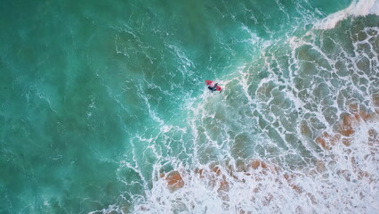 Top view surfer swimming on surfboard waving at foamy ocean. Drone water waves