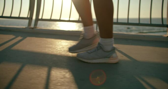 Close up sports shoes woman legs walking on the bridge . Video of athletic legs in the backlight of the sun. Female steps.