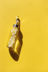 Glass bottle with lemon water drink detox at sunlight on yellow background, copy space. Healthy...