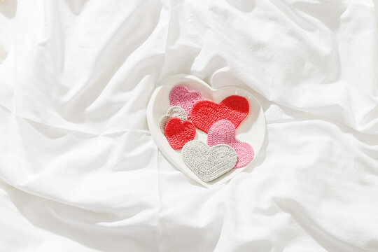 Pink red knitted valentine hearts on bed on white crumpled sheet. Minimal style flat lay photo, Valentine's Day, romantic relationship, love, wedding concept, top view card, tender pastel