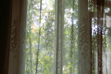 White transparent tulle on the window overlooking the garden. The morning sun illuminates the room.
