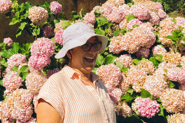 Middle-aged Latin woman laughs next to a pink flower Hydrangea macrophylla in her garden.