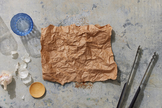 Parchement Paper on Metal Surface with Water Glass, Garlic, Spice dish, and Tongs