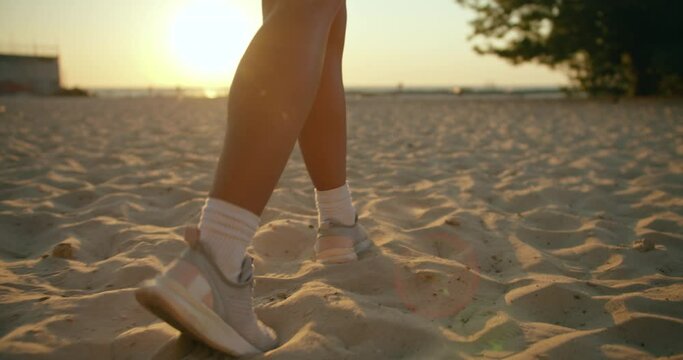 Close up of female feet in sport shoes walking around on golden sand at the beach .