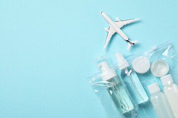 Cosmetic travel kit in plastic bag and toy plane on light blue background, top view with space for...