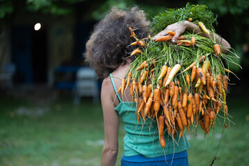 Adult Female Farmer Wearing a Huge Bundle of Organic Carrots on her Shoulder Outdoors