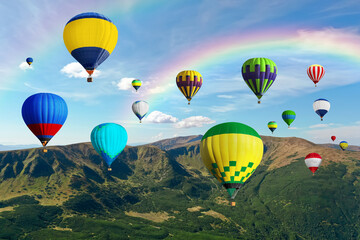 Bright hot air balloons flying in sky with rainbow over mountain