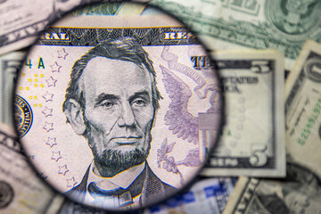 5 American dollar note with Abraham Lincoln face portrait magnified with a magnifying glass, on a background of notes of various denominations. Monetary wallpaper.