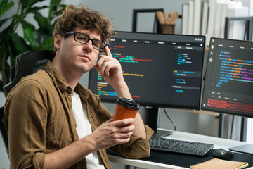 Working IT developer looking at camera holding coffee cup with online software at modern office on...